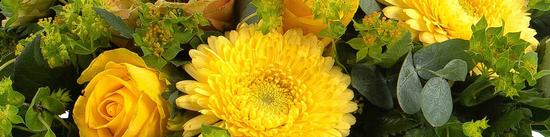 Et farverigt blomsterarrangement med gule gerberaer og roser, omkranset af grønne blade og små blomster. Den varme farvepalette skaber en livlig og glædelig atmosfære.